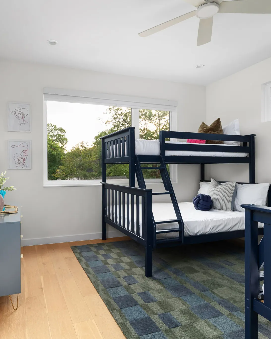 A bunk room with navy bunk beds, a green and blue checked rug, and cowgirl line drawings on the wall