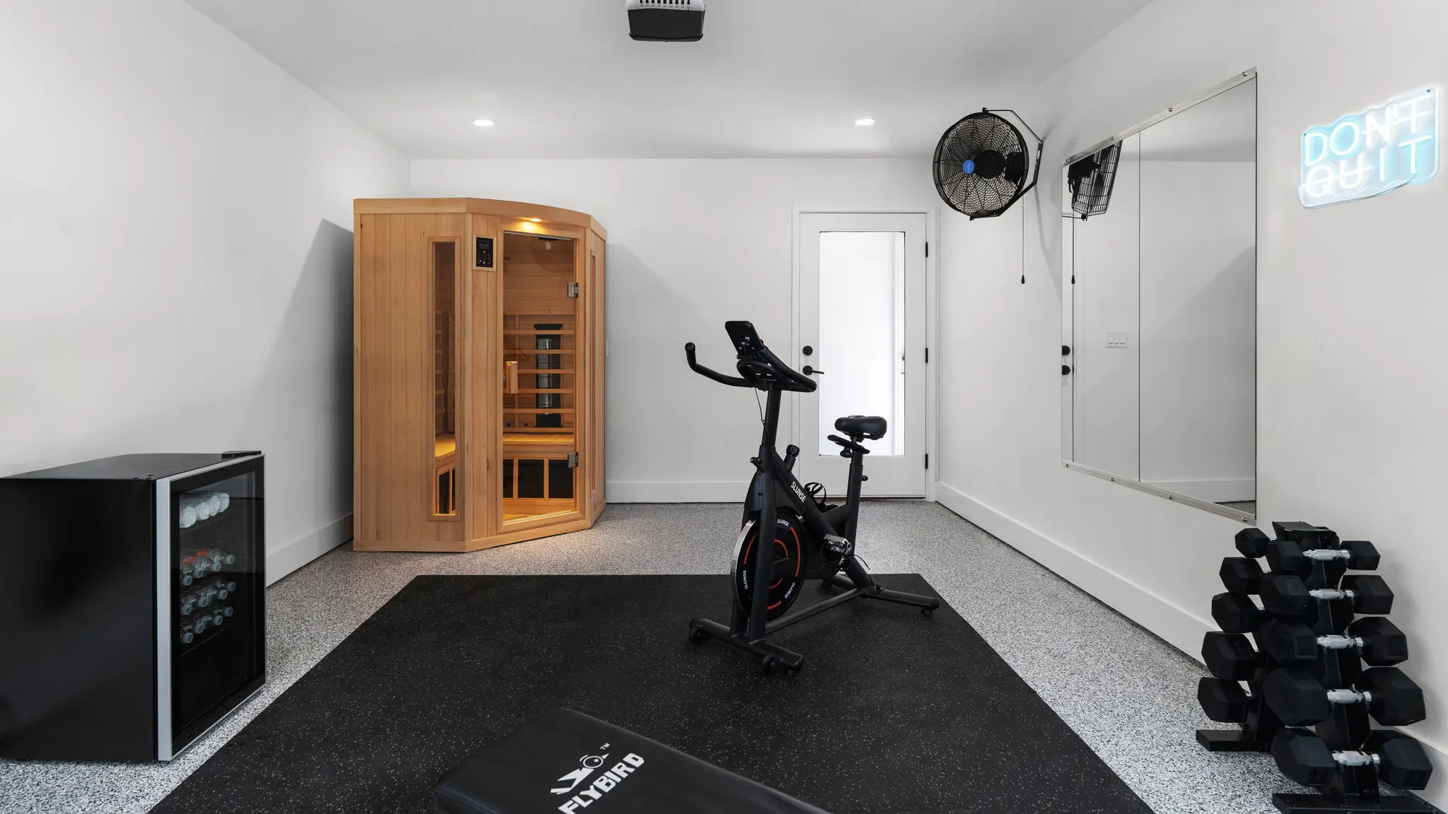 The garage turned gym: an infrared sauna, an exercise bike, a rack of dumbbells and a neon "Don't Quit" sign