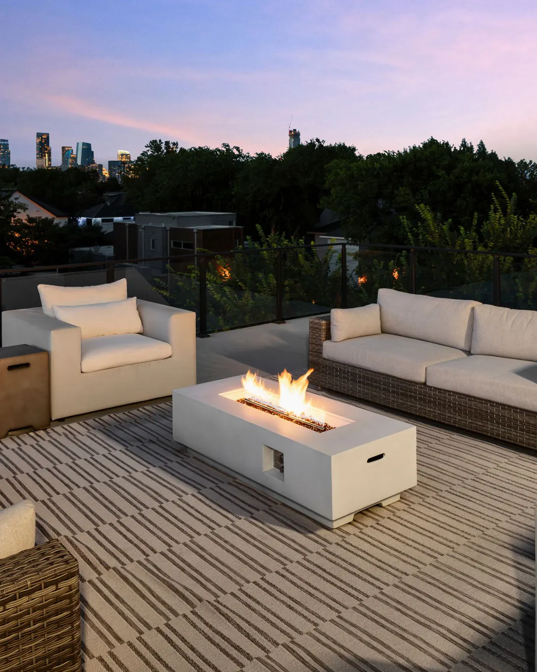 A rooftop deck at dusk with a fire pit, cream outdoor sofas and a view of the downtown Austin skyline
