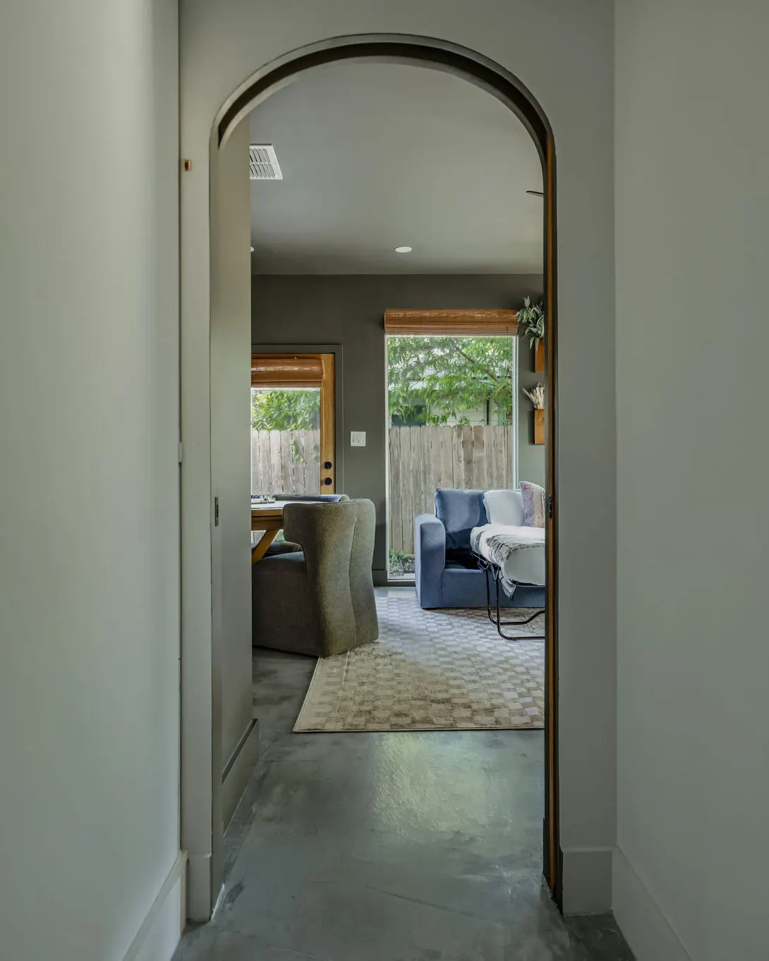 An arched doorway at the end of a hallway, looking into the olive green game room and its blue sofa