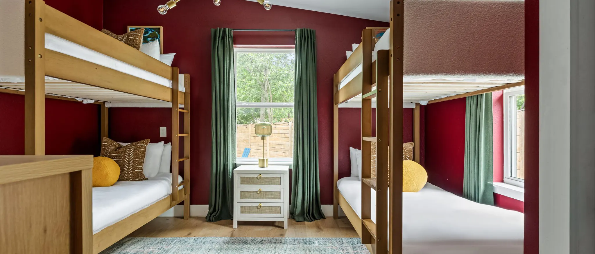 A bunk room with deep red walls, two wooden bunk beds, green curtains and yellow pillows